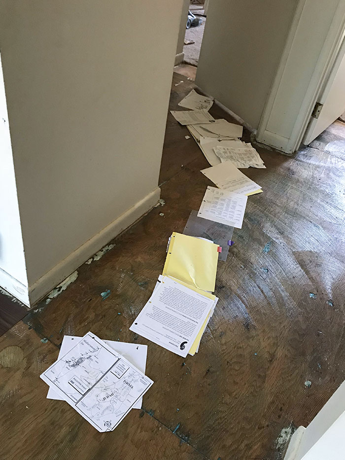 Papers laid out in a hallway on bare wood floor, showing clueless mistake in organizing documents inside a home.