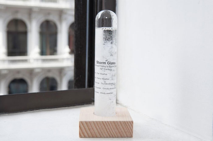 Storm glass weather predictor on a wooden stand near a window.