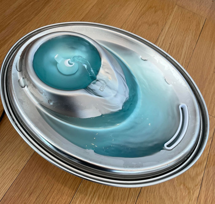 Cat water fountain with blue water on a wooden floor.