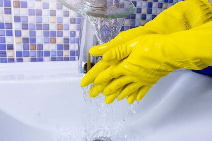 Yellow rubber gloves under running water in a bathroom sink, illustrating hygiene practice. - 4