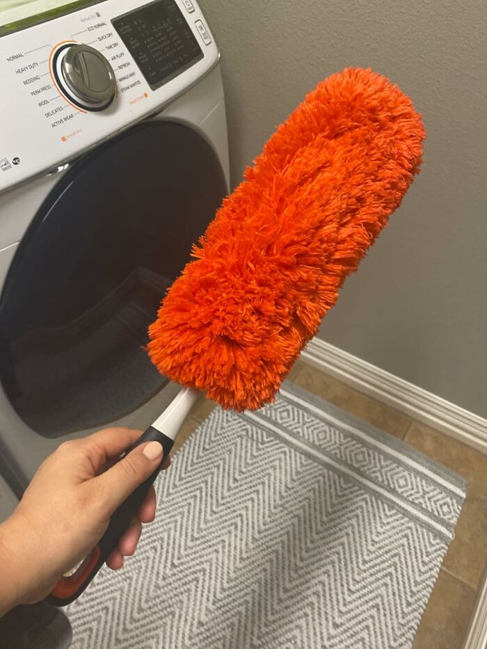 Fluffy orange duster used for deep cleaning a home near a washing machine.