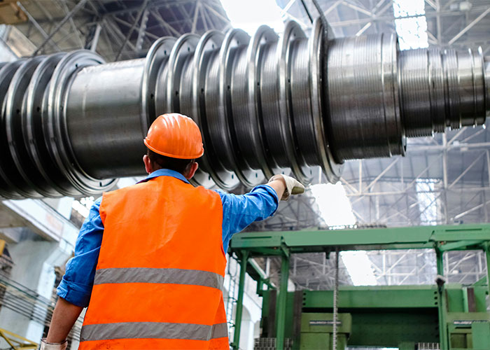 Machinist in an orange vest operating heavy machinery in a factory setting. - 12