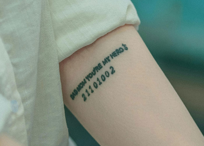 Tattooed arm with numbers and text under a white sleeve, linked to a grandmother's story. - 9