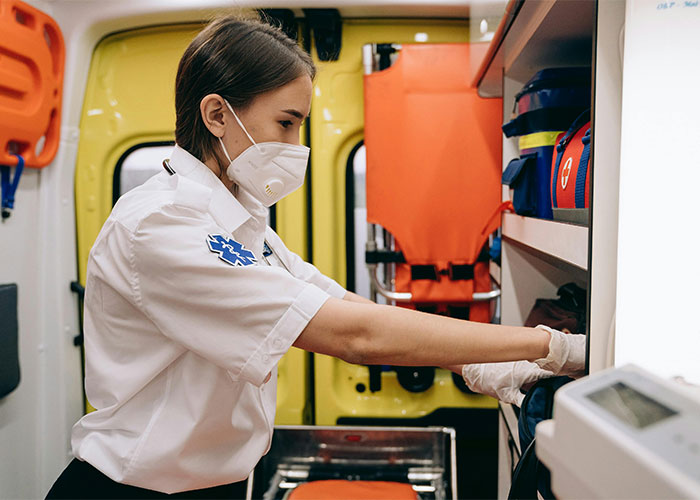 Paramedic wearing a mask organizing medical supplies inside an ambulance, showing a glimpse of emergency life and work.