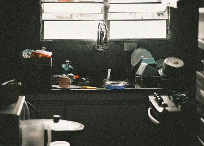 Dimly lit kitchen sink cluttered with dirty dishes and household items, showing a shocked glimpse into how others live.