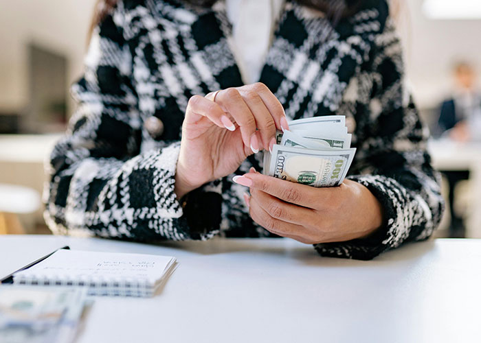 Person counting US dollar bills at a desk, highlighting a shocking glimpse of how others live and manage money.