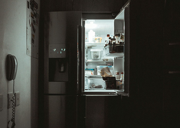 Open refrigerator in a dark kitchen revealing a glimpse inside, showing a surprising view of how others live.