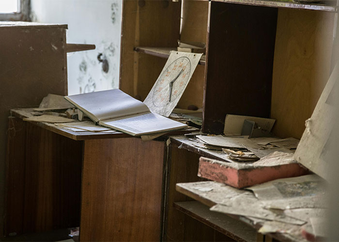 Abandoned room with dust-covered furniture and scattered papers showing shocking living conditions.