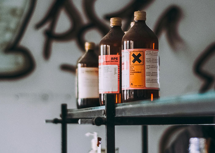 Bottles with warning labels on a metal shelf in a dimly lit room, highlighting shock from how others live.