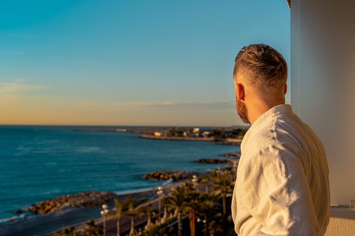 Man in a bathrobe overlooking ocean at luxury resort during sunset, reflecting on employee secrets and stories.