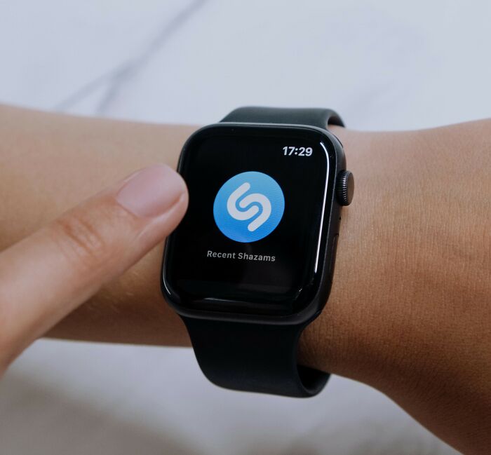 Smartwatch displaying free software app Shazam, a fingertip interacting with the screen.