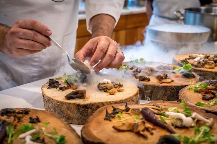 Chef preparing gourmet dishes with smoke on wooden plates, revealing luxury resort employees’ food presentation secrets.