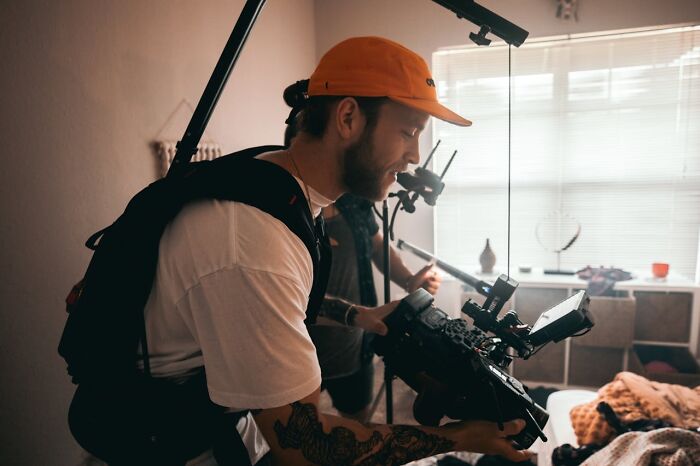 Videographer with orange cap and tattoos filming inside a luxury resort, capturing behind-the-scenes employee secrets.