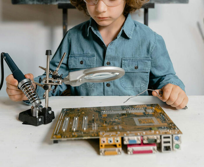 Child in glasses and denim shirt soldering a circuit board, representing creativity and early STEM education. - 28
