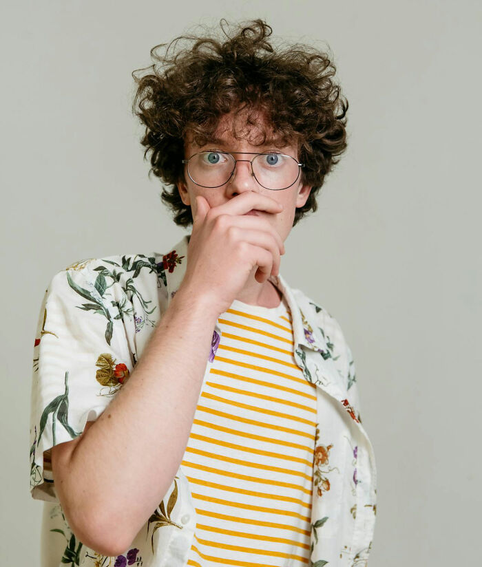 Young man in glasses wearing floral shirt, hand covering mouth, reacting humorously to unfortunate baby names. - 15