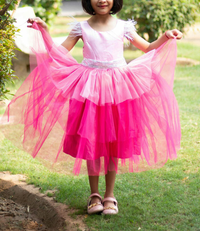 A young girl outdoors in a pink dress holding its sides, showing off an unfortunate yet humorous style choice. - 24