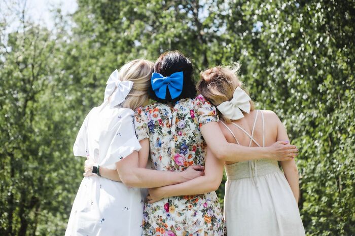 Three women with large bows in their hair, embracing outdoors, showcasing humorously unfortunate fashion choices. - 11