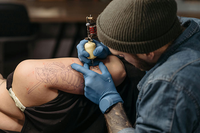 Tattoo artist creating a memorial tattoo, wearing a denim shirt and beanie, focused on detailed work. Tattoo artist creating a memorial tattoo, wearing a denim shirt and beanie, focused on detailed work.