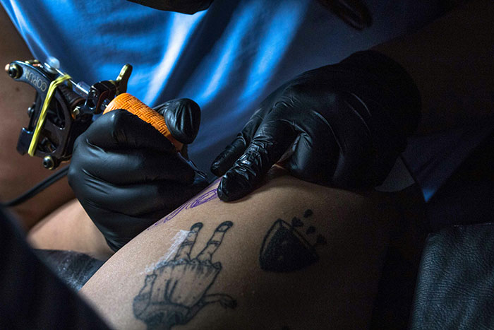 Tattoo artist working on a memorial tattoo, wearing black gloves, using a tattoo machine on a client's arm. Tattoo artist working on a memorial tattoo, wearing black gloves, using a tattoo machine on a client's arm.