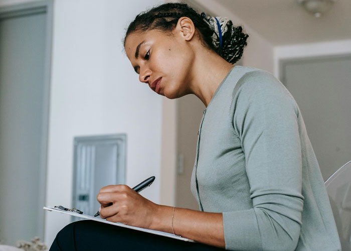 Woman in a green sweater writing on a clipboard, illustrating unique things the rich can purchase unknown to poor people.