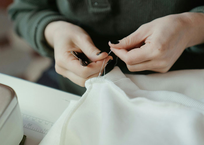 Close-up of hands sewing fabric with a needle, highlighting one of the wildest things the rich can purchase.