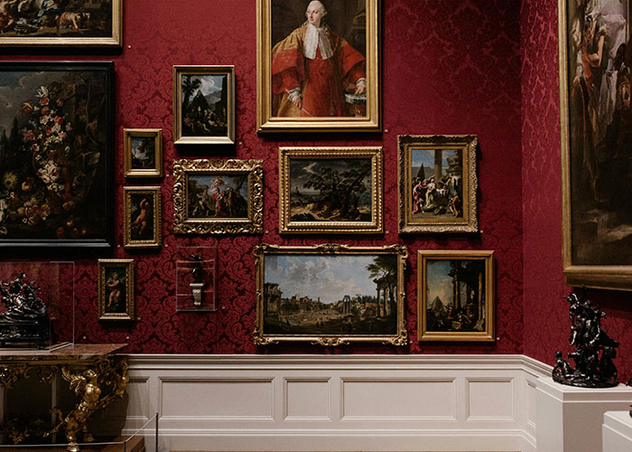 Luxury art collection displayed on red damask walls showcasing some of the wildest things the rich can purchase.