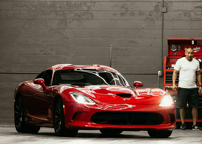 Red luxury sports car in garage with man standing nearby, showcasing wildest things rich can purchase unknown to poor.
