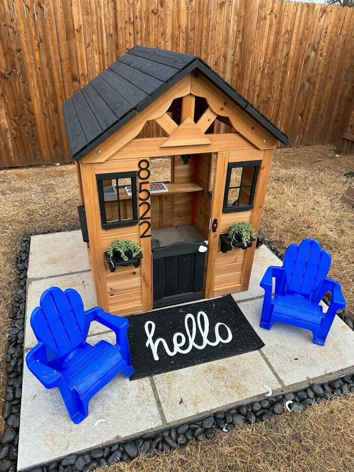 Small wooden playhouse with black roof and two blue garden chairs on a stone patio, a low-effort garden find for beginners.