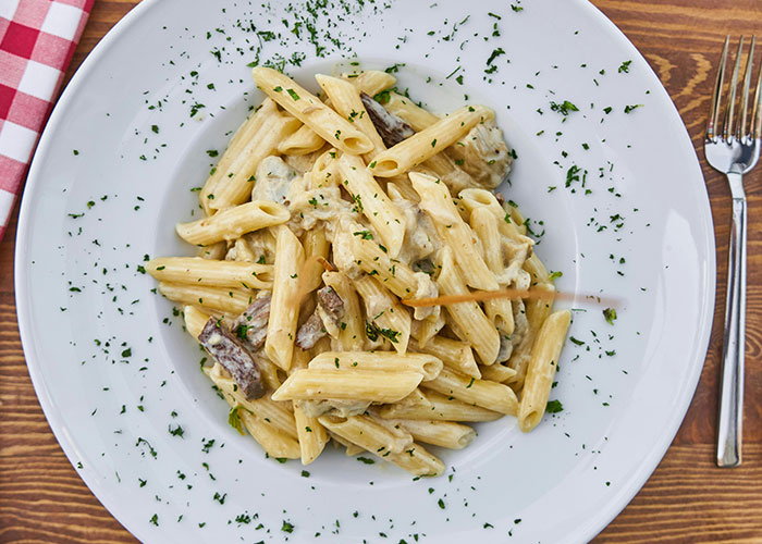 Creamy mushroom penne pasta garnished with herbs on a white plate, showcasing unfiltered food opinions on crunchy vinegar.