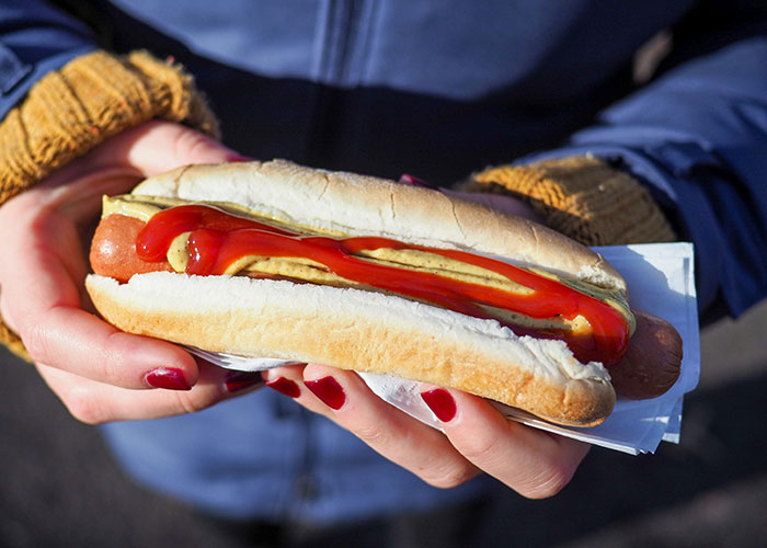 Hand holding a hot dog with ketchup and mustard in a bun, illustrating unfiltered food opinions on crunchy vinegar.