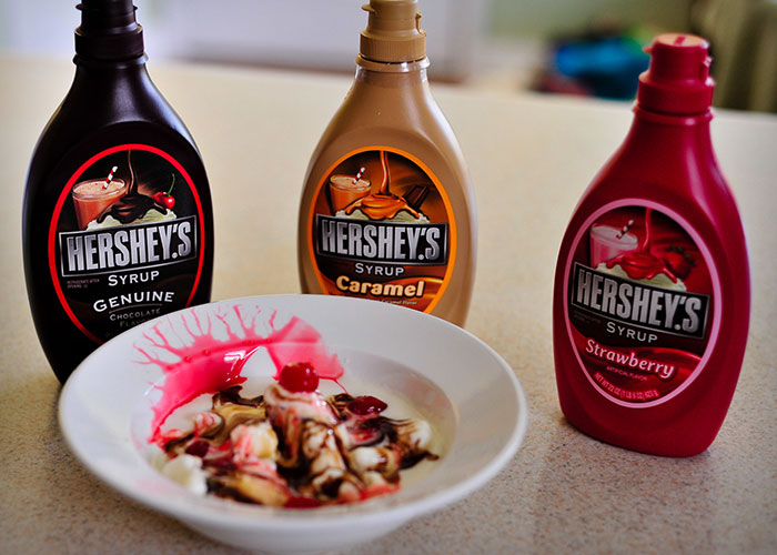 Bottles of Hershey's syrup in chocolate, caramel, and strawberry flavors with a dessert drizzled with syrups.