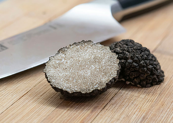 Close-up of fresh black truffles cut open on a wooden board next to a chef's knife, highlighting gourmet food opinions.