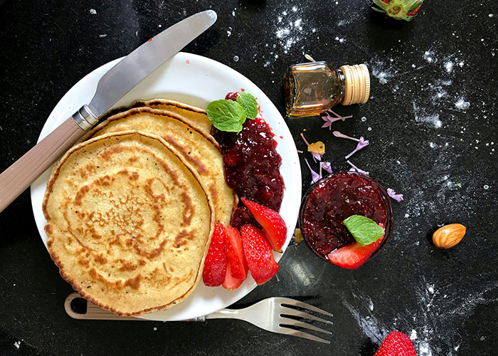 Plate of pancakes with strawberry jam and fresh strawberries on a black surface, showcasing crunchy vinegar food opinions.