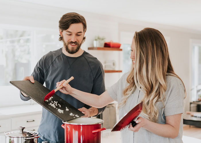 Husband attempts a cooking surprise for wife on Mother's Day, guiding ingredients into a pot together.