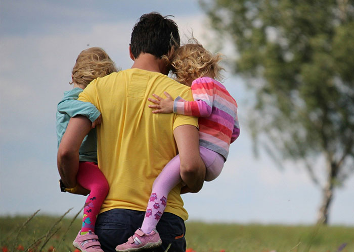 Man carrying two young children outdoors, illustrating strange childhood realities people later learned were far from normal.