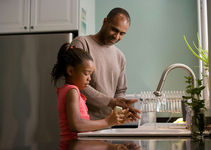 A father and daughter washing hands together in a kitchen, illustrating strange childhood realities people later learned.