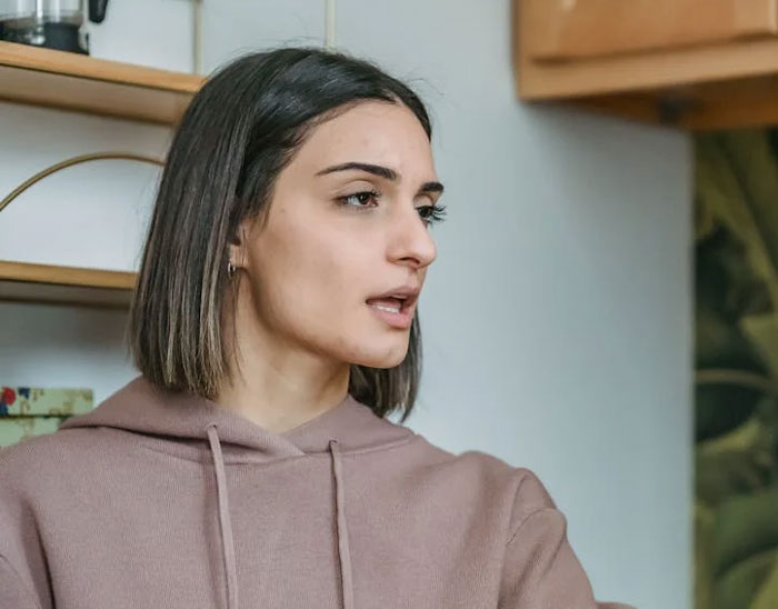 Woman in a beige hoodie looking to the side, expressing surprise and emotion.