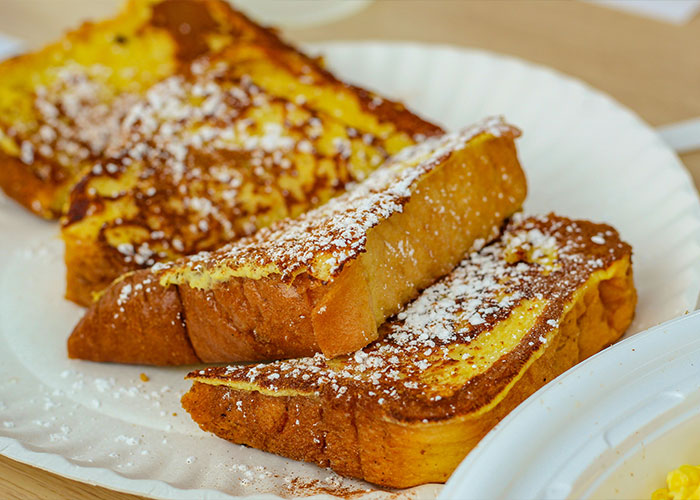 Close-up of three slices of French toast sprinkled with powdered sugar on a white paper plate, childhood food memories concept.