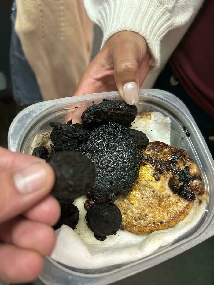 Burnt food dish in a container, held by a person in a light sweater, showcasing an unusual culinary creation.