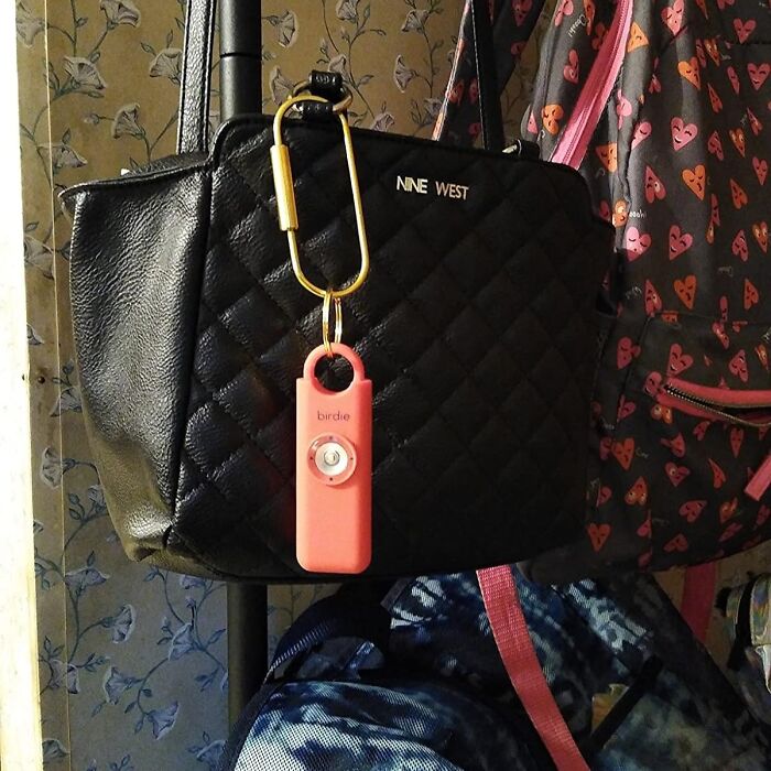 Black quilted Nine West handbag with a pink novelty keychain hanging on a hook among other colorful bags.