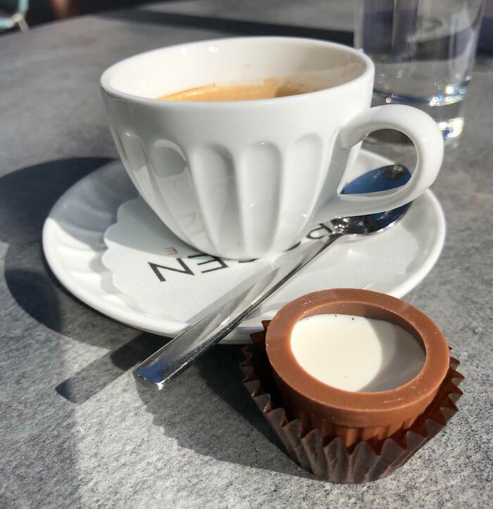 White ceramic cup of coffee with a spoon on saucer and a chocolate dessert in a creative bar or restaurant setting