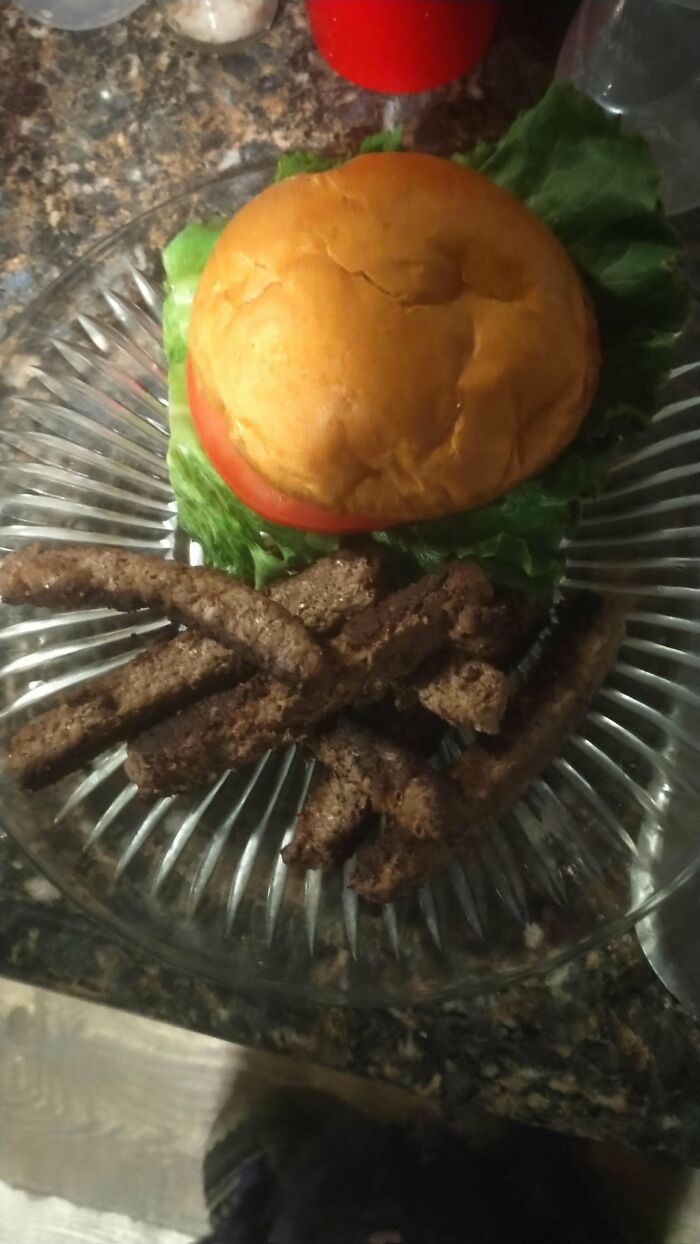 Unusual dish with a burger and fried breadsticks on a glass plate.