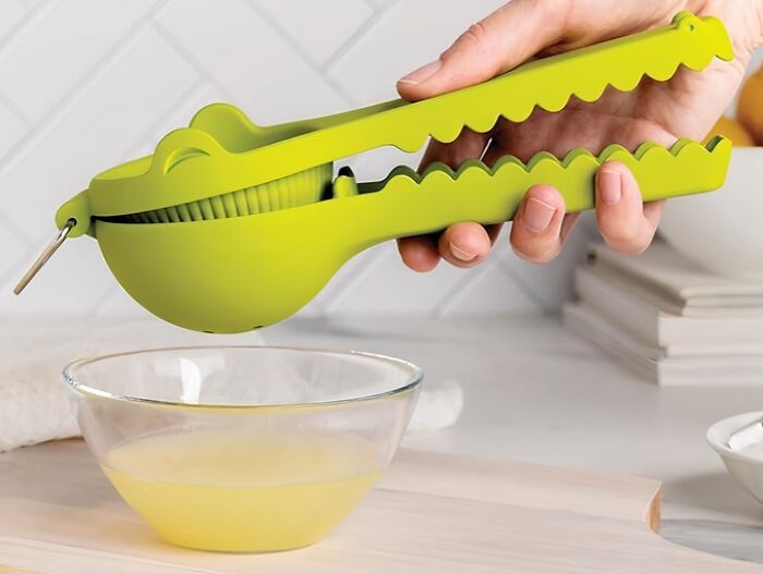 Green alligator-shaped lemon squeezer in action over a glass bowl, showcasing a weird kitchen item that works well.