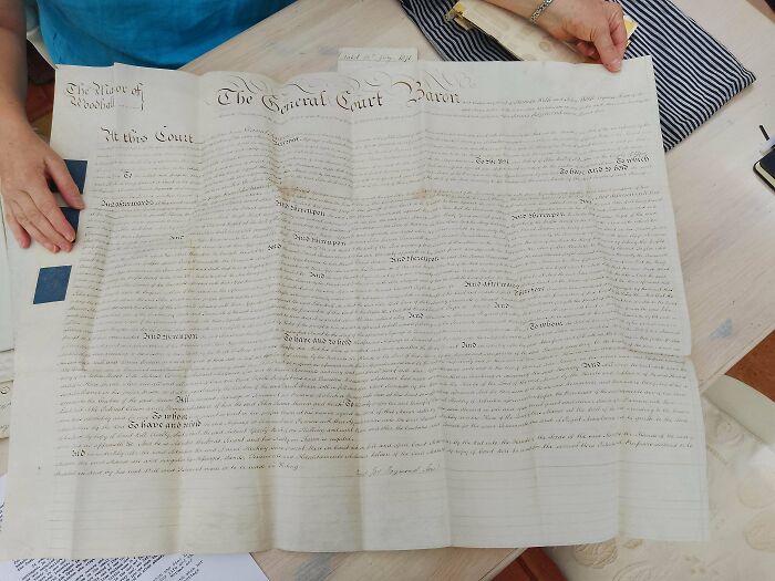 A person holds an old UK legal document on a table, showcasing British heritage.