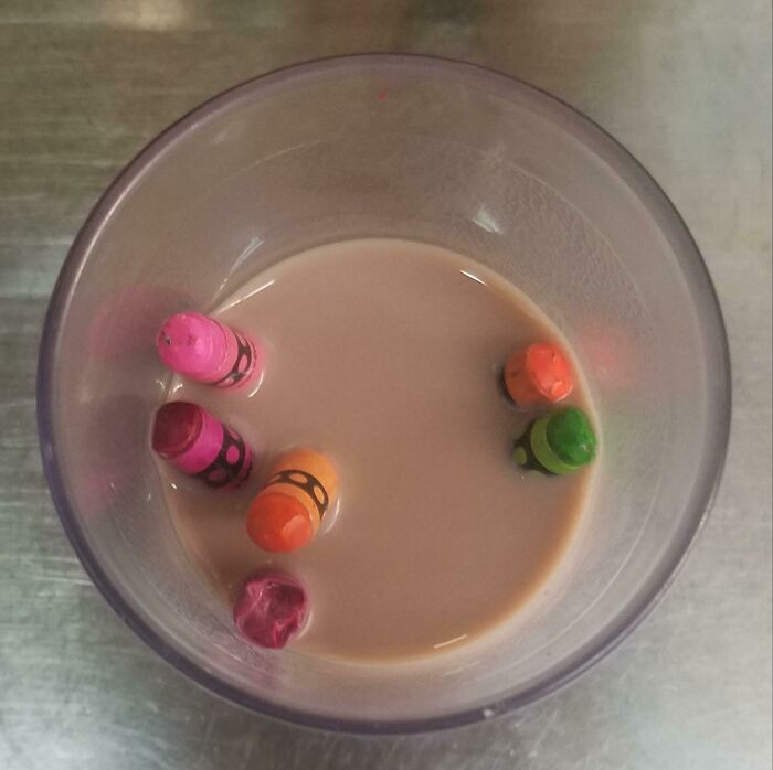 Glass of chocolate milk with colorful crayons soaked inside, illustrating parents having a pretty miserable day.