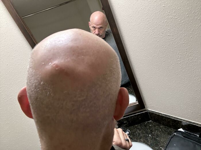 Bald man looking into bathroom mirror with a frustrated expression, capturing parents having a pretty miserable day.