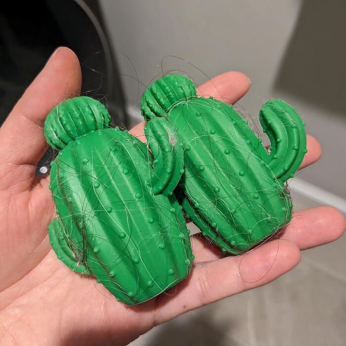Hand holding two green cactus-shaped hair removers covered in hair, useful everyday finds to fix annoyances.