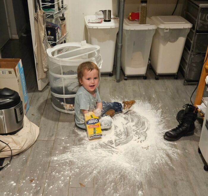 Toddler sitting on kitchen floor covered in spilled corn starch, illustrating parents having a pretty miserable day moment.