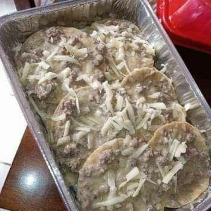 Unappetizing food photo: tortillas with grayish sauce and cheese in a foil tray.