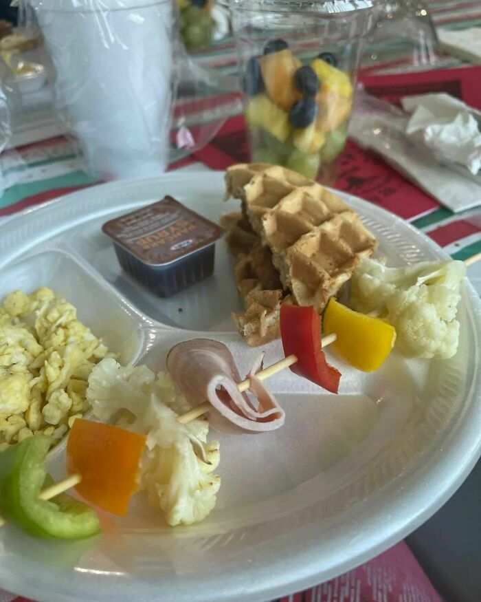 Unappetizing food on a plate with waffles, scrambled eggs, and skewered ham with vegetables.